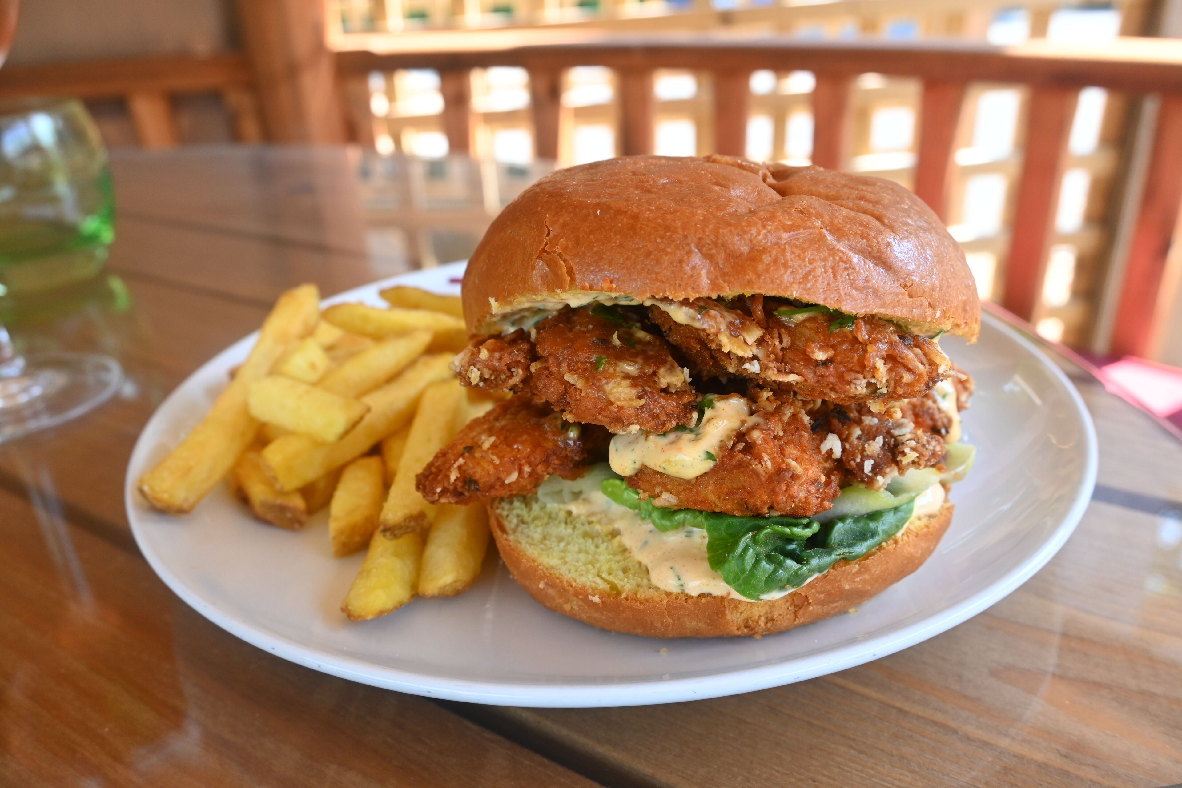 A plate with a chicken sandwich and French fries on a table.