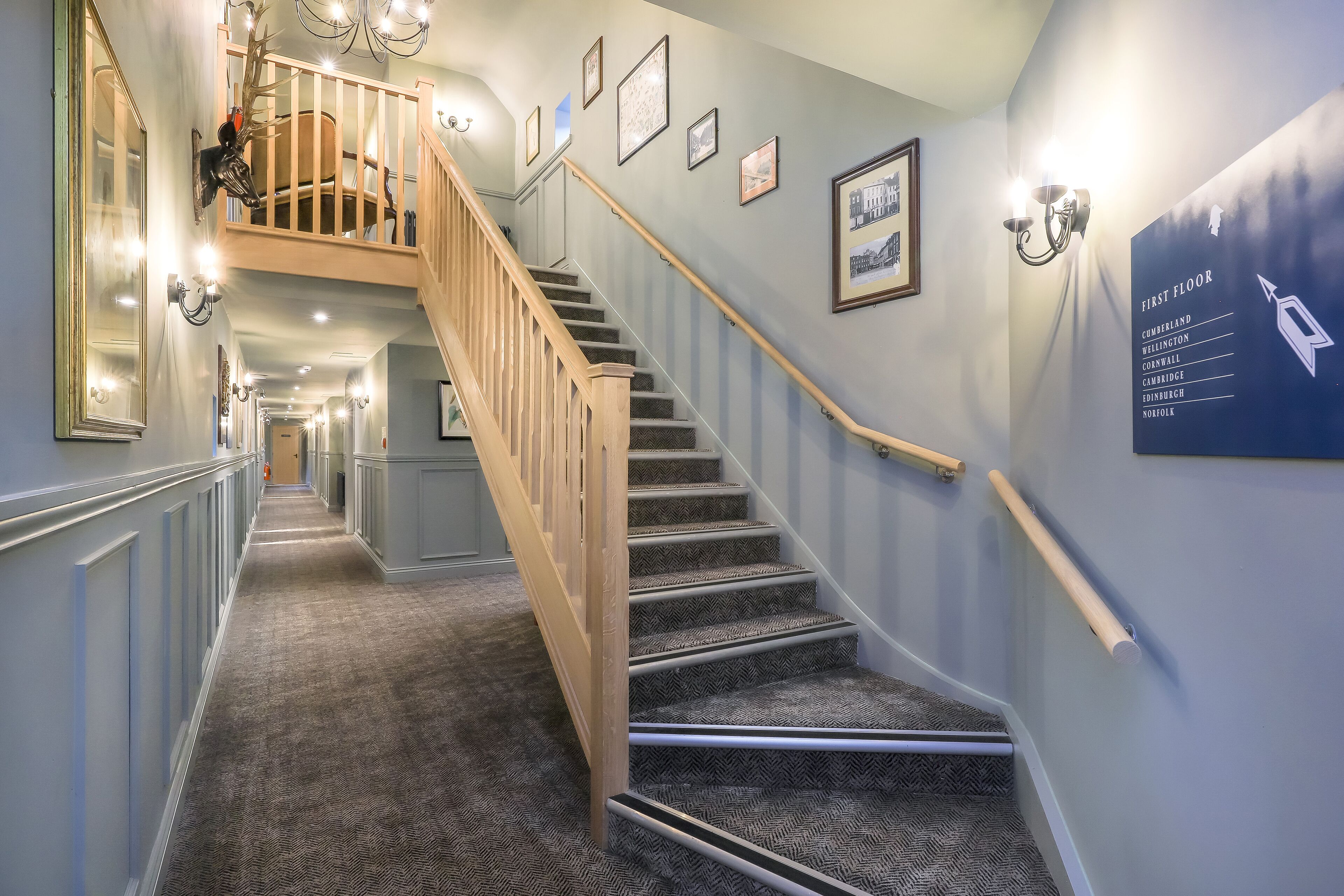 A hallway with a staircase, framed pictures, and a sign indicating the first floor.