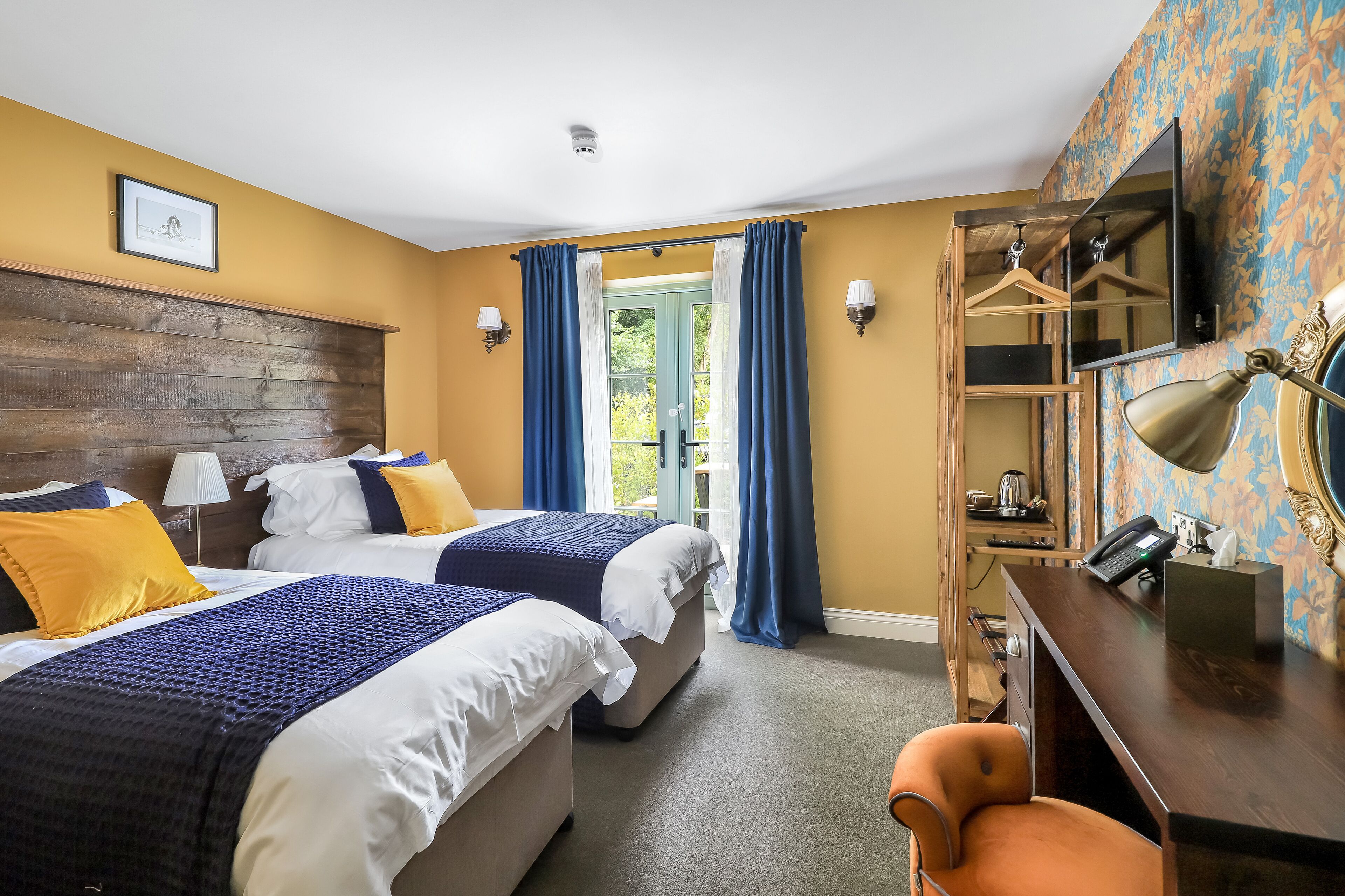 A hotel room with two beds, a desk, a chair, a wardrobe, and a large window with curtains.