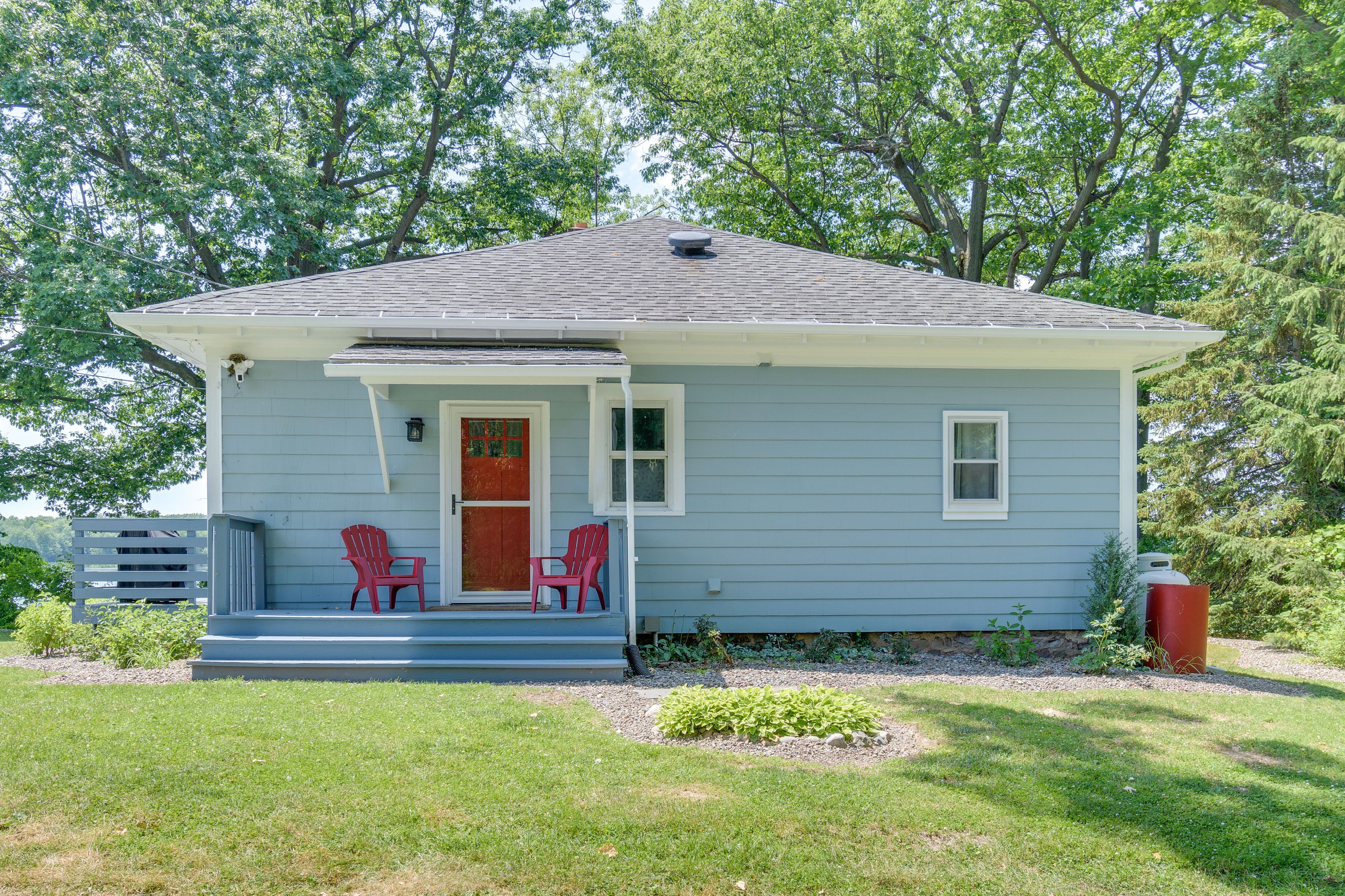 A small house with a porch, two red chairs, and a red door.