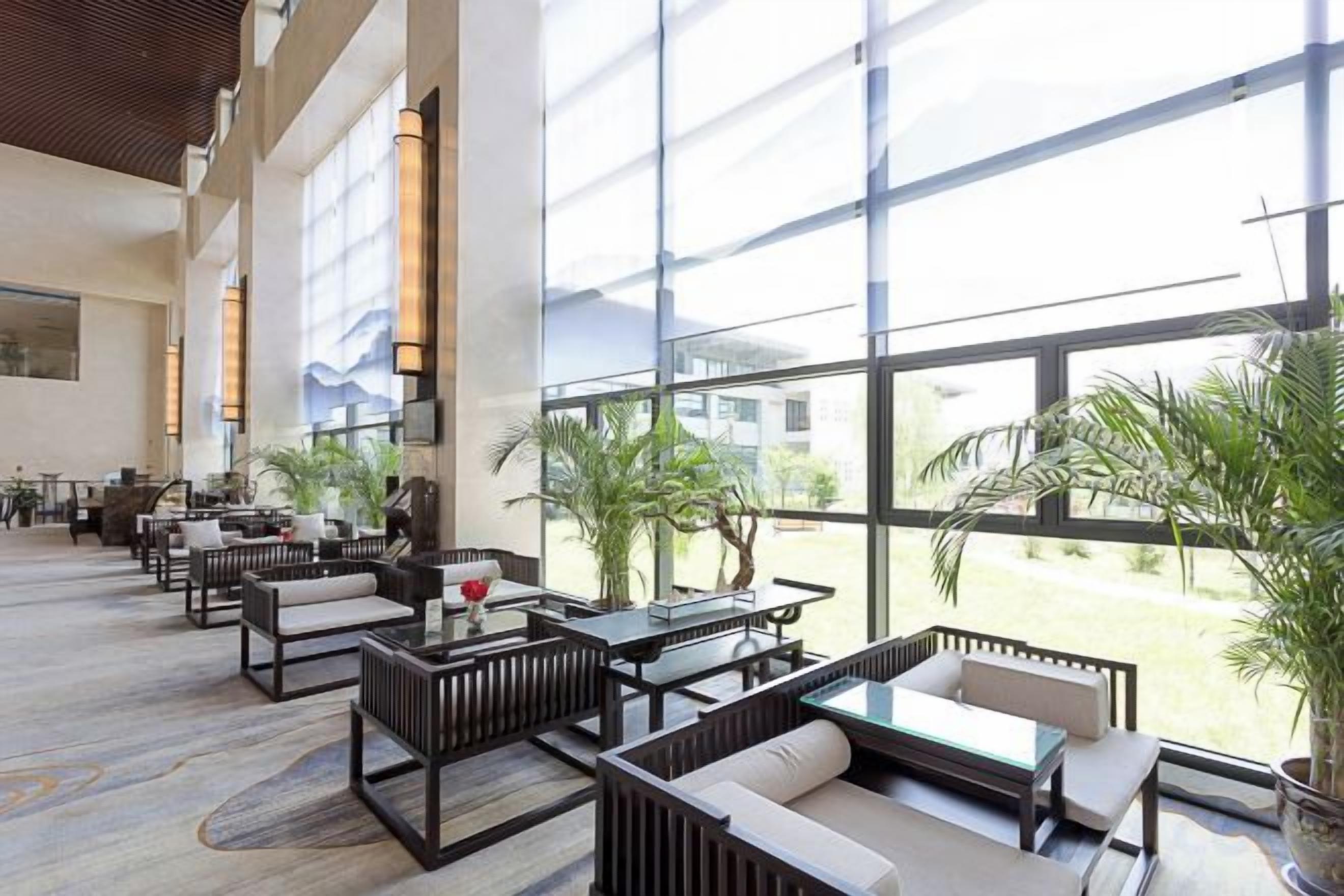 A spacious indoor area with multiple seating arrangements, large windows, and potted plants.