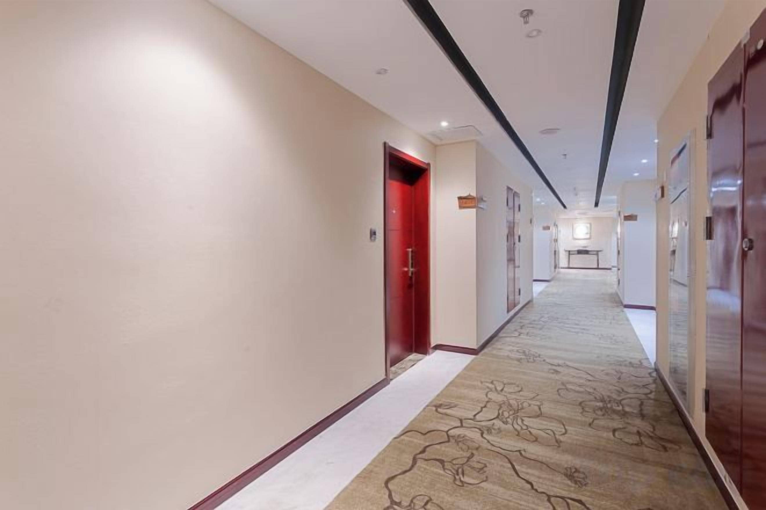 A hotel corridor with a carpeted floor, doors, and a hallway leading to a room.