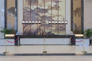 A reception area with a marble counter, red ropes, and a large wall mural. - Nanshanyuan Hotel (Xi'an)