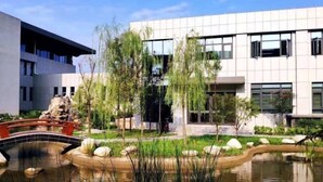 A modern building with a reflective glass facade, a small bridge over a water feature, and surrounding greenery. - Nanshanyuan Hotel (Xi'an)