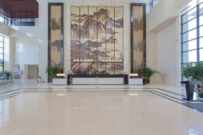 Un vestíbulo amplio con un mural grande, una recepción y plantas en macetas.