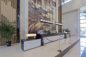 Un mostrador de recepción con una barrera de cuerda roja, un mural grande en la pared y una planta en maceta a la izquierda.