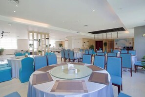 A spacious dining area with round tables and blue chairs, a kitchen in the background, and a large window providing natural light. - Nanshanyuan Hotel (Xi'an)