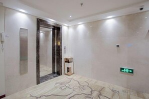 Un ascensor moderno con puerta de vidrio, piso de mármol y señal de salida verde.