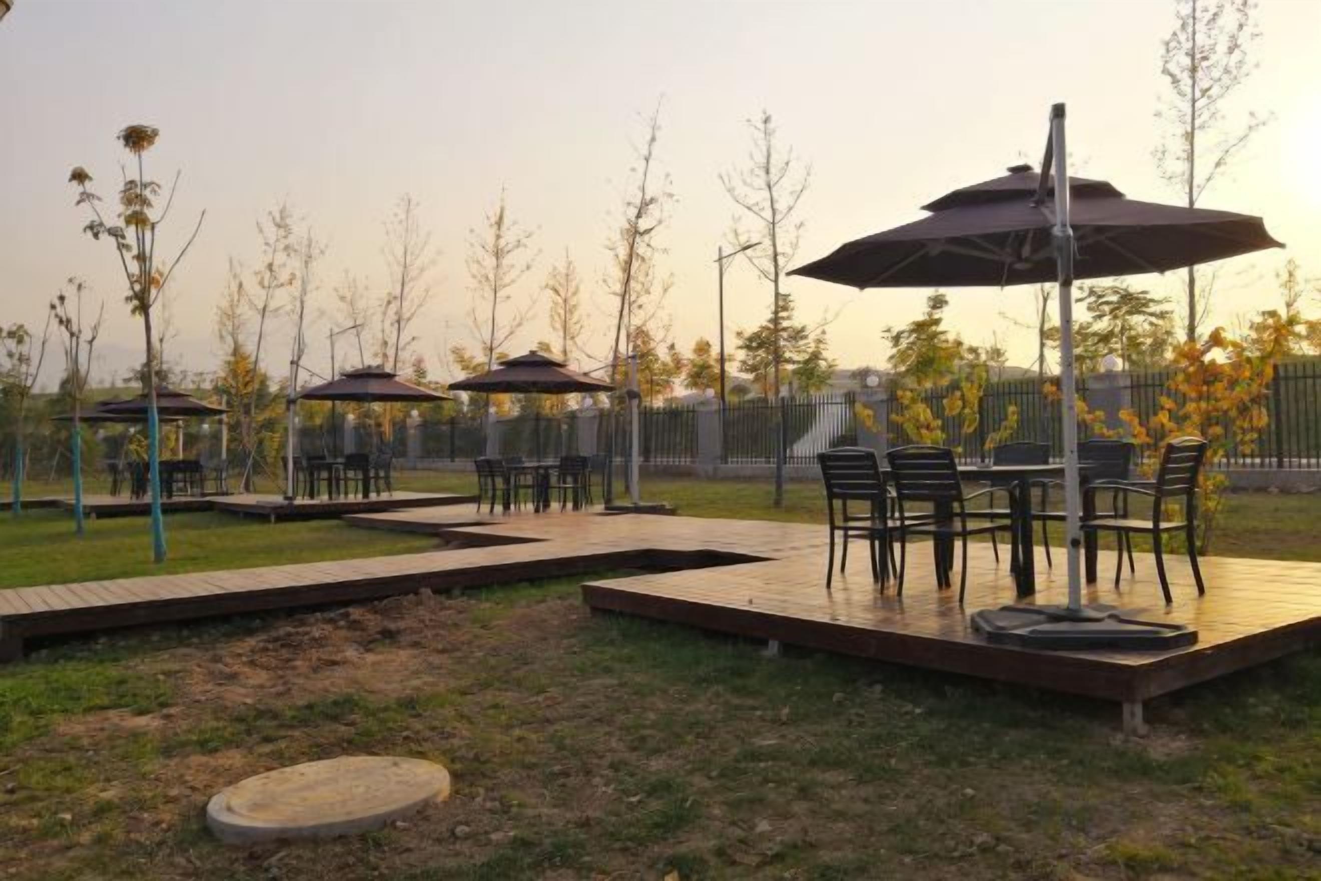 An outdoor patio area with tables and chairs, surrounded by a fence and trees.