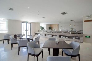 Un comedor moderno de hotel con mesas y sillas, una barra de cocina y un ventanal grande.