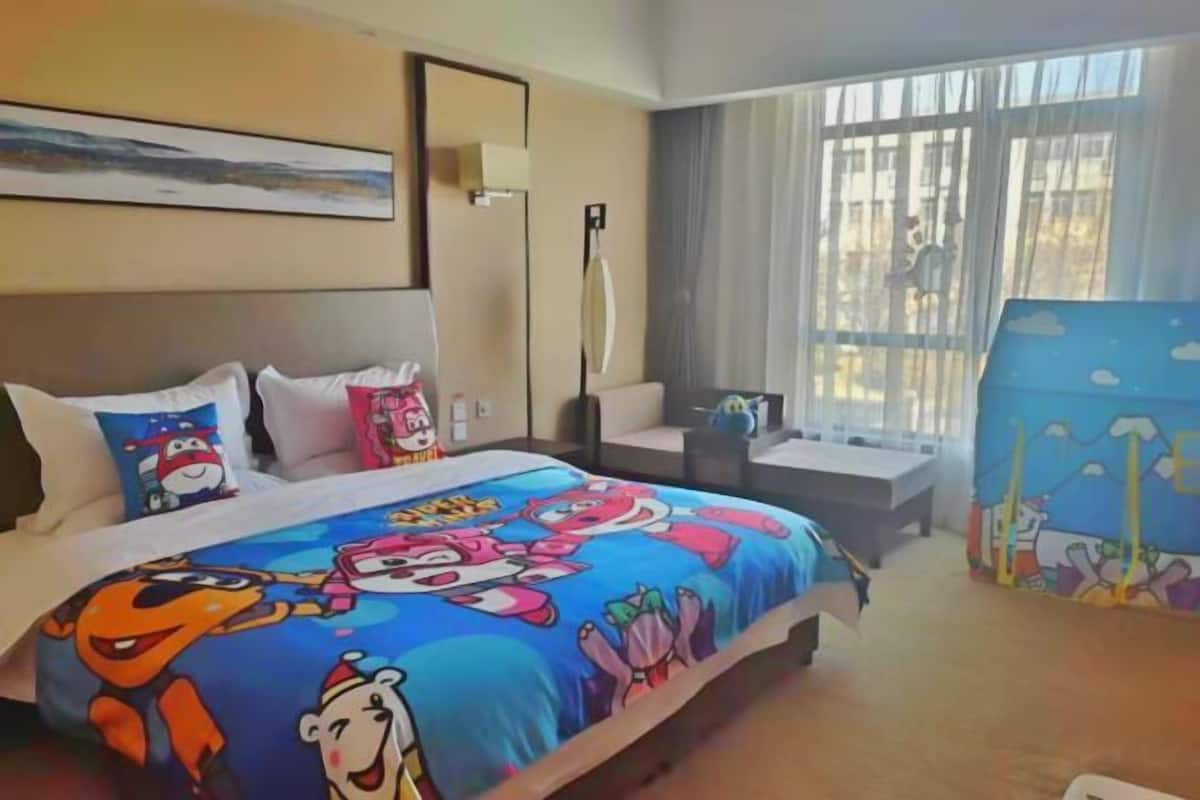 A hotel room with a bed, a desk, a chair, a lamp, and a window with curtains.