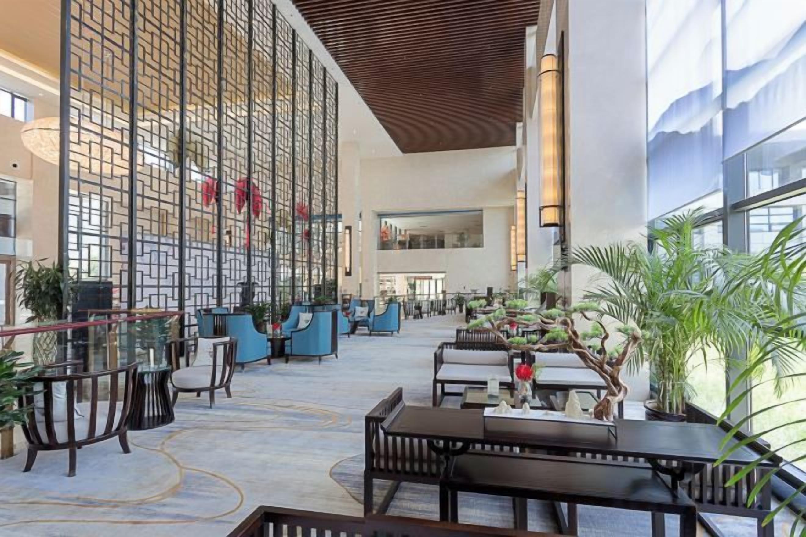 A spacious lobby with seating areas, a large wall with vertical elements, and a large window providing natural light.