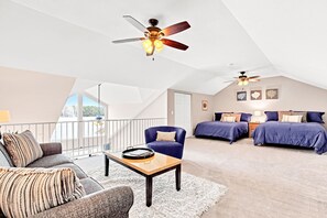 Amplio dormitorio tipo loft con una cama grande, una zona de estar con sofá y sillón, y un ventilador de techo.