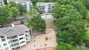 Ein mehrstöckiges Gebäude mit Balkonen, einem Schwimmbad und einer Sandfläche mit Schaukeln.