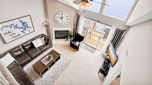 Ein geräumiges Wohnzimmer mit einer braunen Ledersofa, einem Couchtisch, einem Kamin und einem großen Fenster mit Blick auf ein Gewässer.