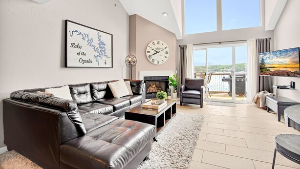 Ein modernes Wohnzimmer mit einer Ledersofa, einem Couchtisch und einem Kamin. An der Wand hängt eine große Uhr und ein Gemälde zeigt einen See.
