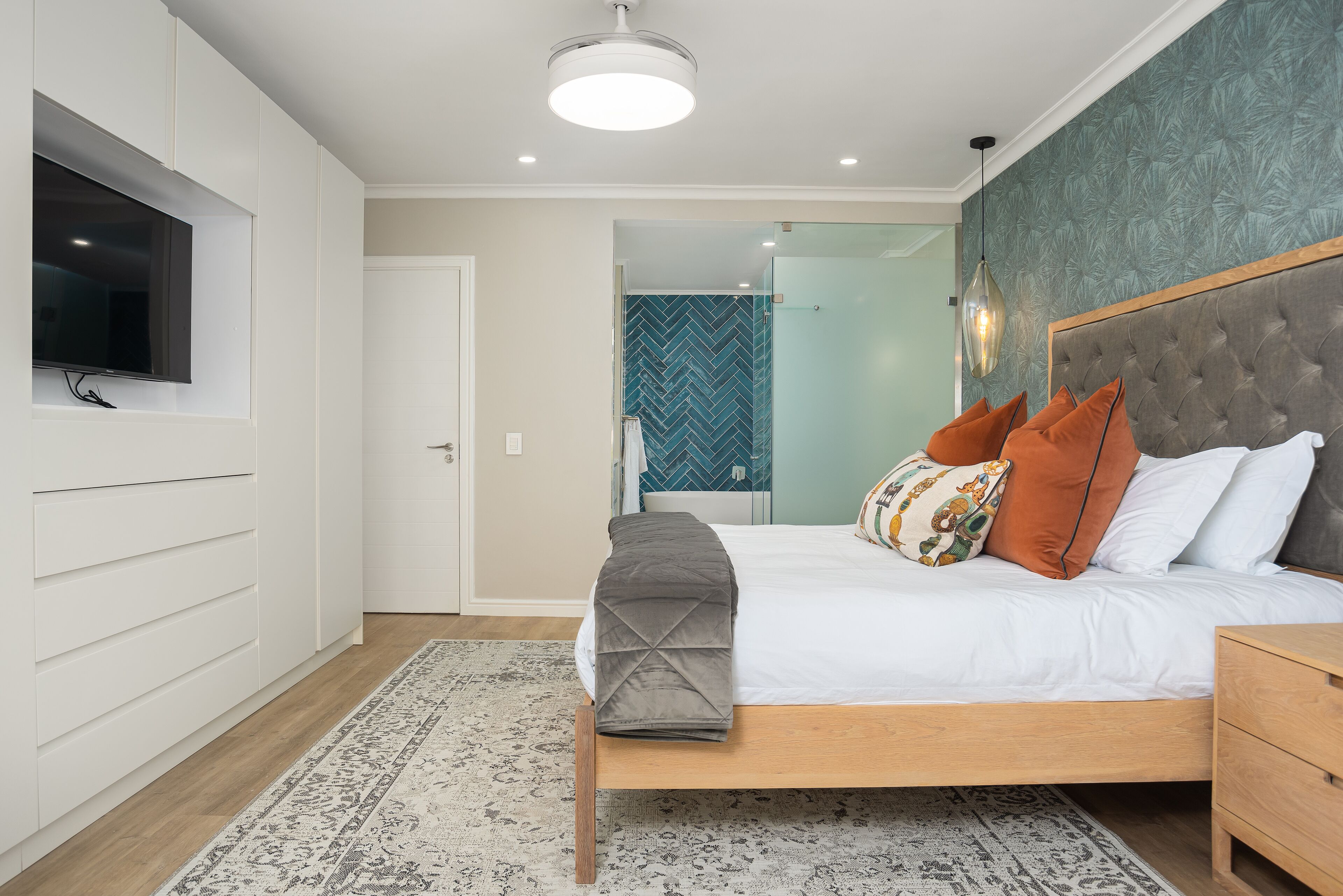 Un dormitorio moderno con cama, mesitas de noche, televisor y una alfombra estampada.