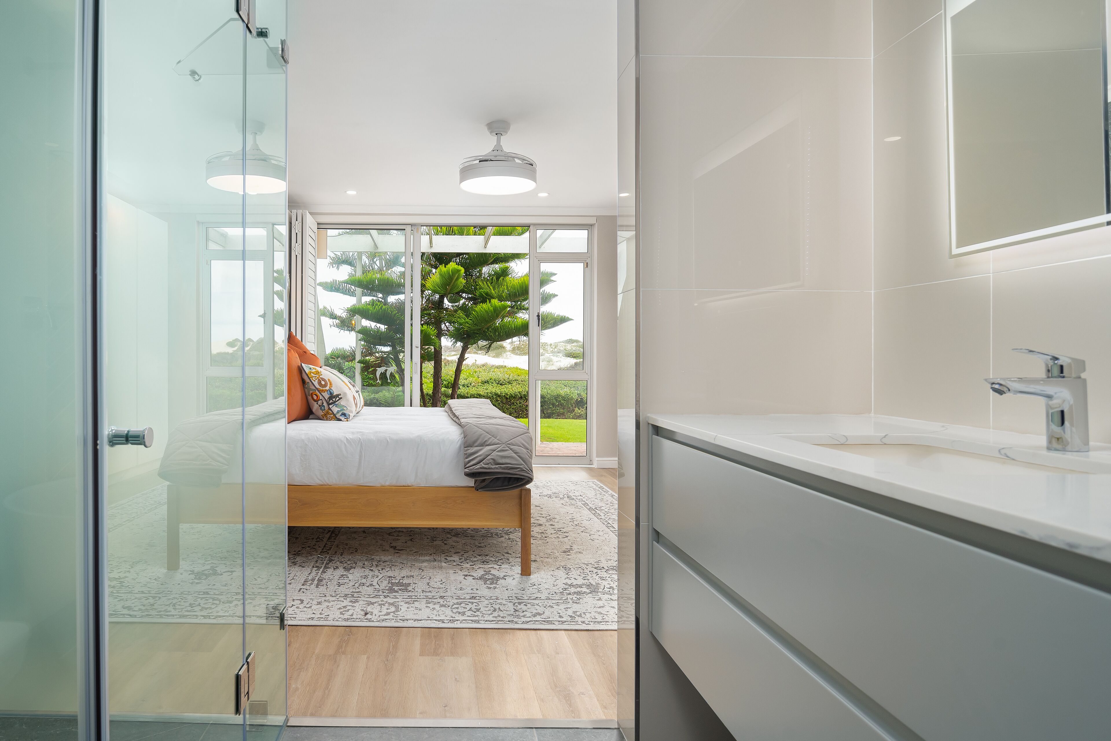 A modern bedroom with a large bed, a glass door leading to a balcony, and a bathroom with a large mirror and sink.
