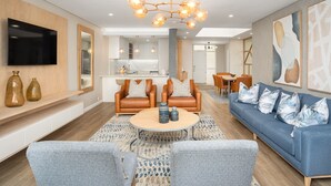 Una sala de estar moderna con un sofá azul, dos sillones de cuero marrón, una mesa de centro redonda y un televisor montado en la pared.