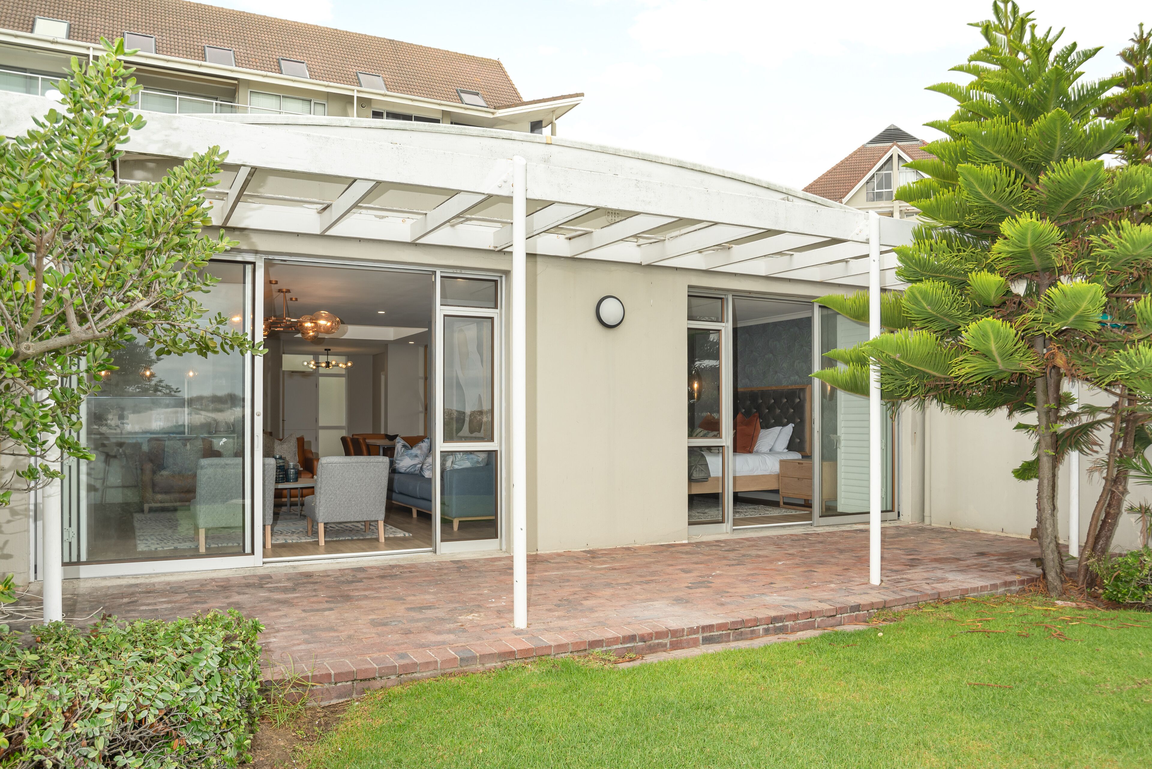 Una casa moderna con patio coperto, ampie vetrate e prato curato.