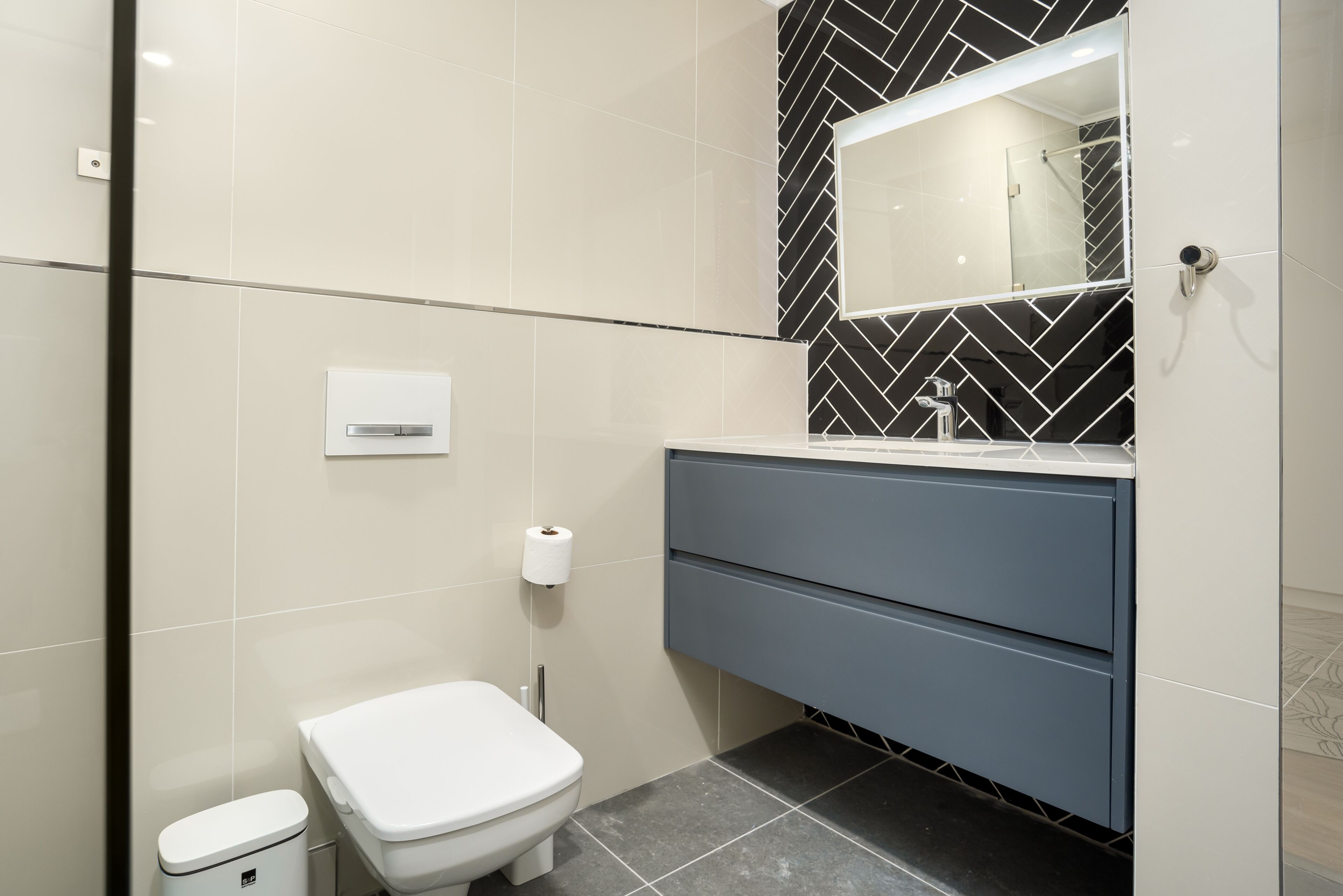 Un baño moderno con inodoro, lavamanos con espejo y un perchero para toallas.