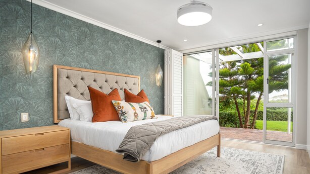Un dormitorio con una cama de madera, una mesita de noche, un ventanal y vistas al verdor exterior.