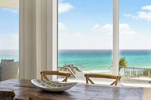A dining area with a view of the ocean, a wooden table, and two chairs.