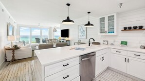 Una cucina moderna con mobili bianchi, una grande isola, illuminazione a sospensione e vista all'esterno.