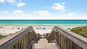 Una passerella di legno che conduce a una spiaggia con ombrelloni blu e un cielo azzurro limpido.