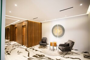 A modern waiting area with a wooden panel wall, two armchairs, a round table, and a unique wall art piece.