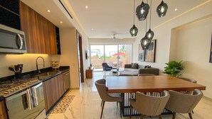 A modern kitchen with a large island, a dining area with a wooden table and chairs, and a living space with a sofa and a TV. - NEW large balcony, hot tub, gym (Puerto Vallarta)