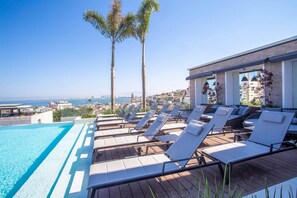 A poolside area with lounge chairs and a view of the city and sea.