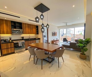 A modern kitchen with wooden cabinets, a built-in microwave, and a dining area with a marble floor and a wooden table.