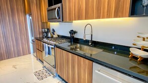 A modern kitchen with wooden cabinets, a black countertop, stainless steel appliances, and a patterned floor. - NEW large balcony, hot tub, gym (Puerto Vallarta)