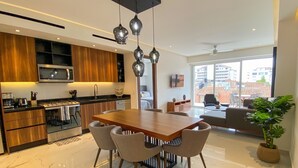 A modern kitchen with wooden cabinets, a stainless steel microwave, and a dining area with a marble floor and a wooden table. - NEW large balcony, hot tub, gym (Puerto Vallarta)