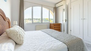 Une chambre à coucher comprenant un lit, une commode, une fenêtre en arc de cercle et une armoire.