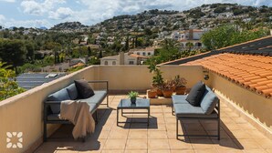 Une terrasse sur le toit, aménagée avec deux canapés, une petite table et des plantes en pot. La terrasse offre une vue sur une colline parsemée de nombreuses maisons.