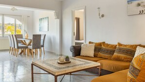 Un salon spacieux comprenant un coin repas, un canapé agrémenté de coussins à motifs et un tableau accroché au mur.