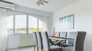 Un espace repas moderne avec une table en verre et des chaises à revêtement gris, une grande fenêtre avec des rideaux et un ventilateur de plafond.