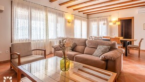 Un salon comprenant un canapé, des fauteuils, une table basse en verre et un vase avec des fleurs séchées.