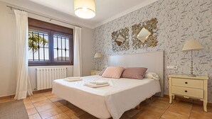 Une chambre à coucher avec un grand lit, deux tables de chevet, une fenêtre avec des rideaux, un radiateur et un papier peint à motifs floraux.