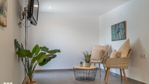 A modern living room with a flat-screen TV mounted on the wall, a large potted plant, two wicker chairs with cushions, and a small round coffee table. - Villa CORASOL by Abahana Villas (Teulada)