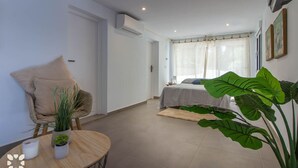 A modern hotel room with a bed, a sitting area with a chair and a small table, and a large potted plant. - Villa CORASOL by Abahana Villas (Teulada)