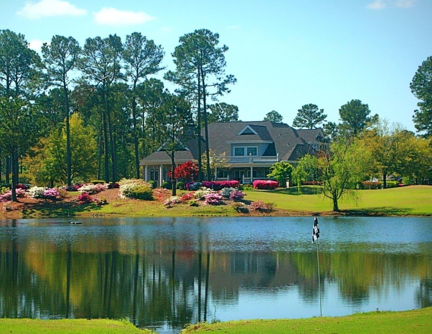 A large house with a pond in front, surrounded by trees and landscaped gardens.