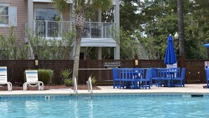 A swimming pool with lounge chairs and umbrellas, a fence, and a building in the background. - 1204l Home by Redawning (Calabash)