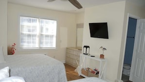 A bedroom with two beds, a dresser, a television, and a window with blinds.