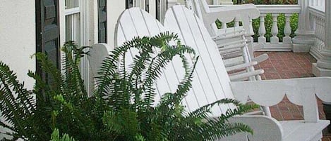 A porch with white chairs and a potted fern.