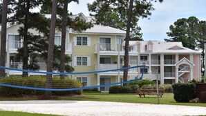 A multi-story building with balconies, a grassy area in front, and a hammock.