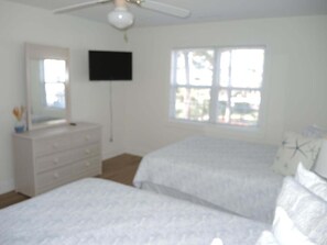 Een slaapkamer met twee bedden, een dressoir, een aan de muur bevestigde televisie en een raam.
