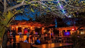 Ein Restaurant im Freien mit Holztischen und -stühlen, einer Bar und stimmungsvoller Beleuchtung.
